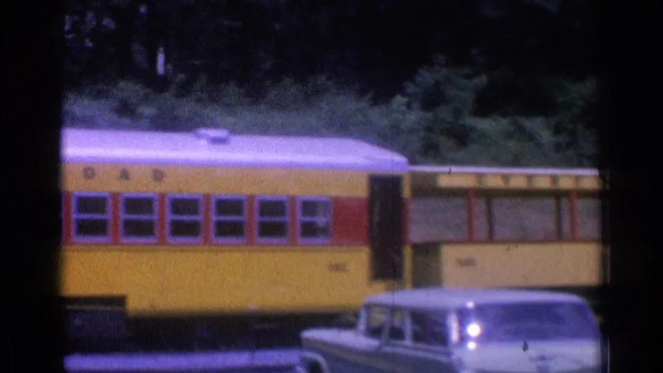 Yellow train cars and a light-colored older automobile appear in a 1976 Chicago rail station view.