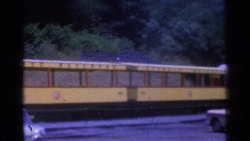 A yellow rail car continues past tracks and trees in the final frame of the 1976 Chicago home movie clip.