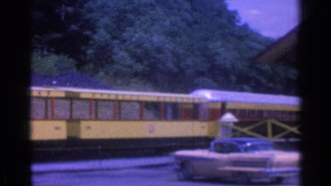 Yellow train cars beside a museum station with a classic car in the foreground.