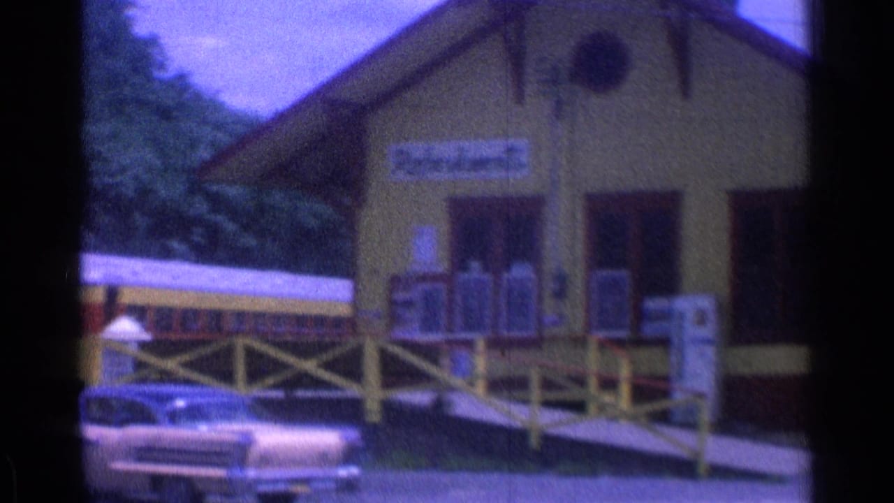 Yellow museum station building with train cars and a parked classic car nearby.