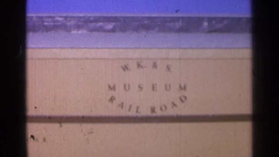 1976 home-movie frame showing WK&S Museum Railroad lettering below the station scene, with train cars and platform details above.