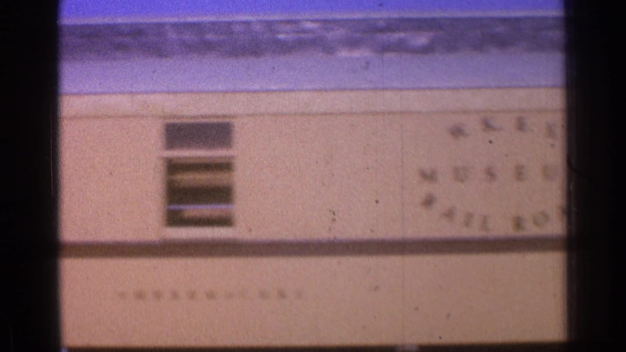Beige building facade with blue roof edge, window openings and faded wall lettering.