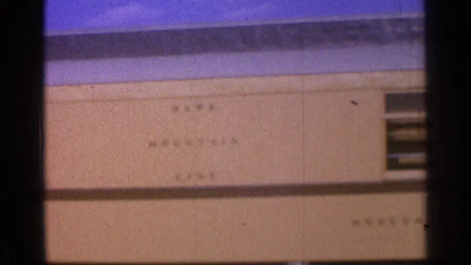 1976 8mm frame showing a circular sign that appears to read museum railroad on a beige exterior wall.