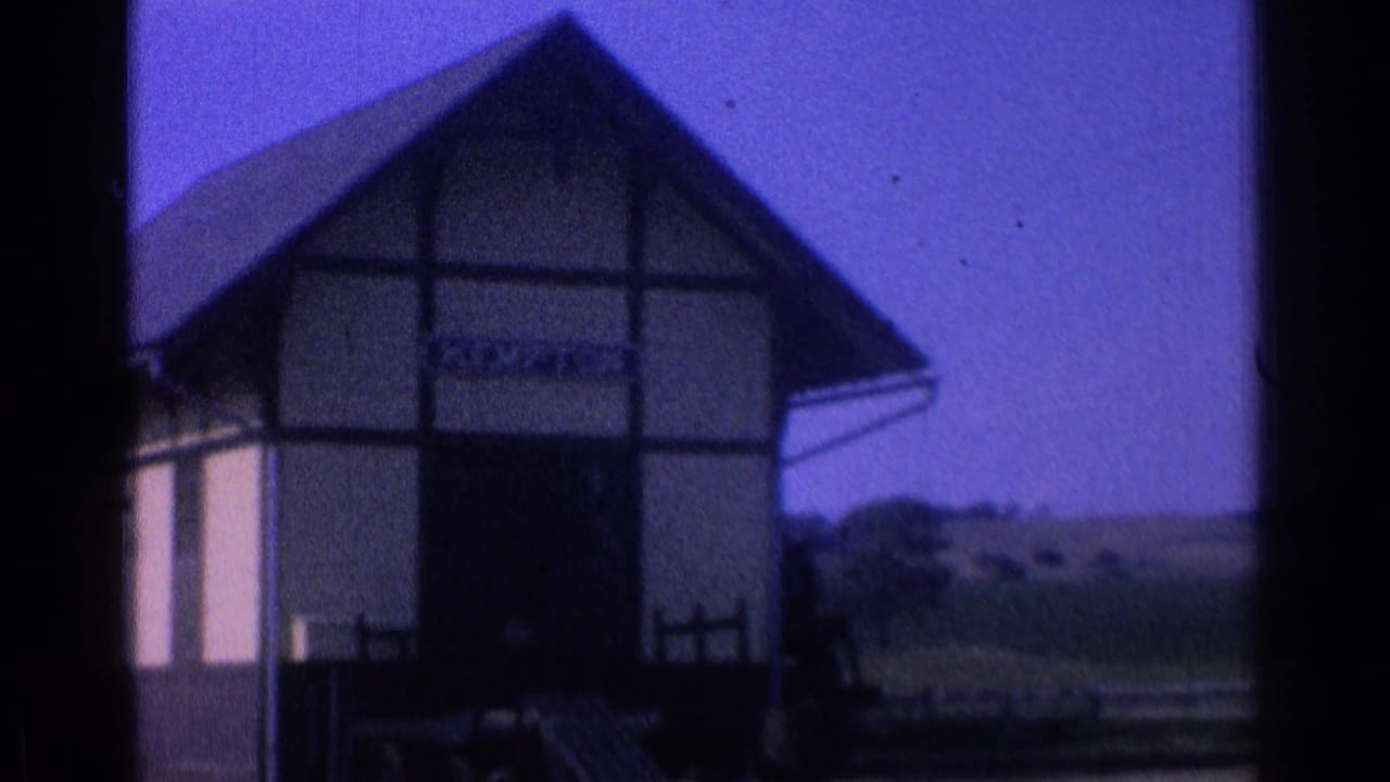Timber-framed station building with a partially readable station sign and countryside beyond.