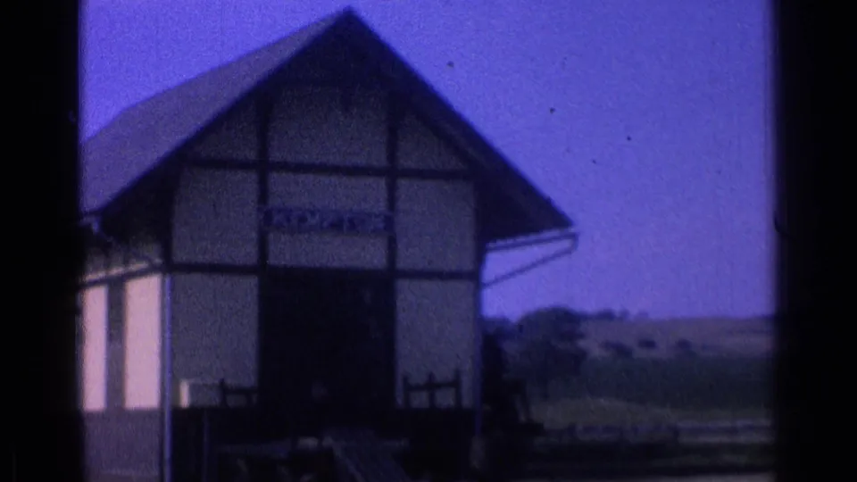 1976 8mm frame showing a gabled timber-framed station building, platform area, and partially readable Kempton-style sign.