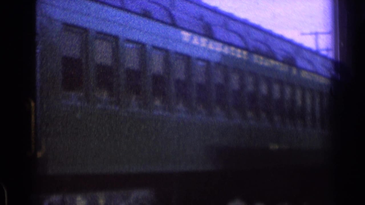 Passenger car side with windows and painted lettering near a station building.