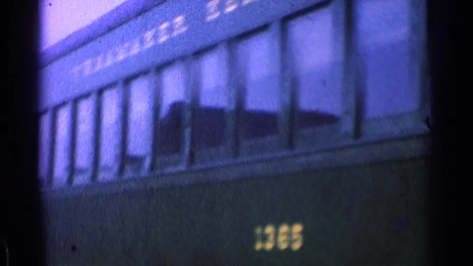 Close 8mm frame of a dark green passenger car showing windows, painted lettering, and the number 1365.