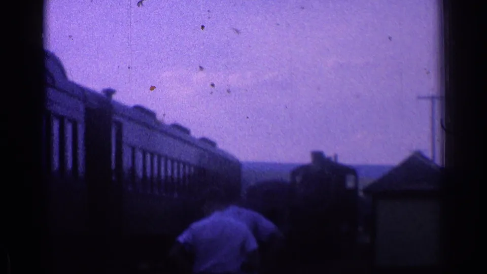 1976 home-movie frame showing people near passenger cars and a small station structure in Illinois.