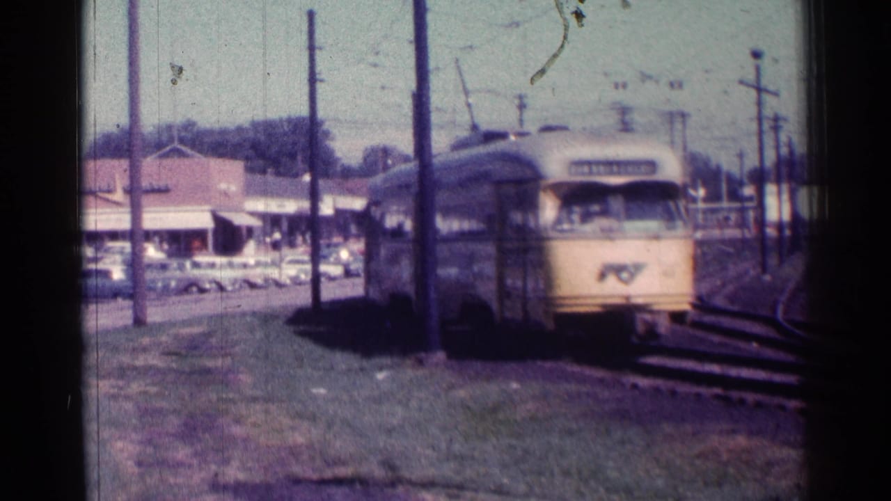 Yellow rapid transit train approaches on tracks beside utility poles and storefronts.