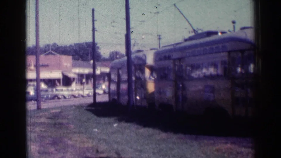 1976 Chicago street scene with yellow rapid transit cars moving past the camera near shops, poles, and parked automobiles.