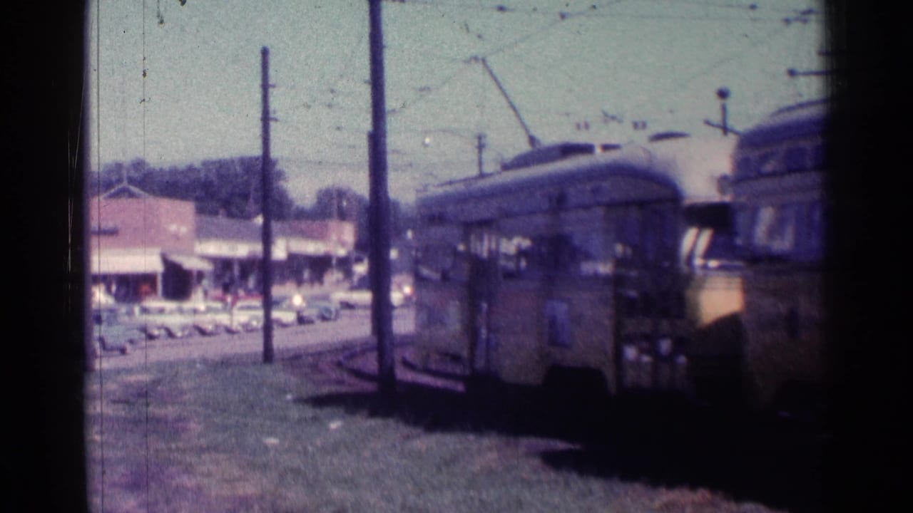 Yellow trolley passing along curved tracks beside storefronts and parked cars.