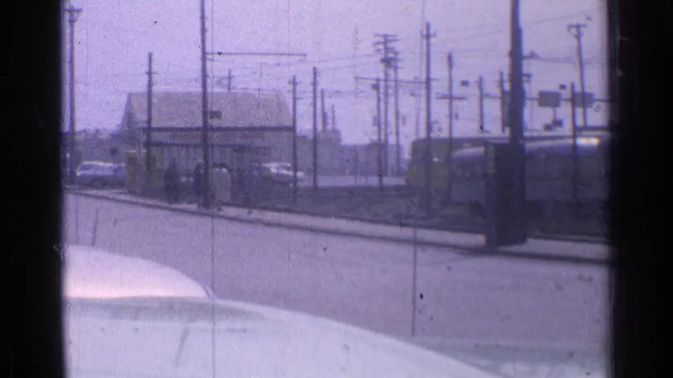 Chicago street view from 1976 with rail infrastructure, utility poles, a low building, parked cars, and the trolley near frame edge.