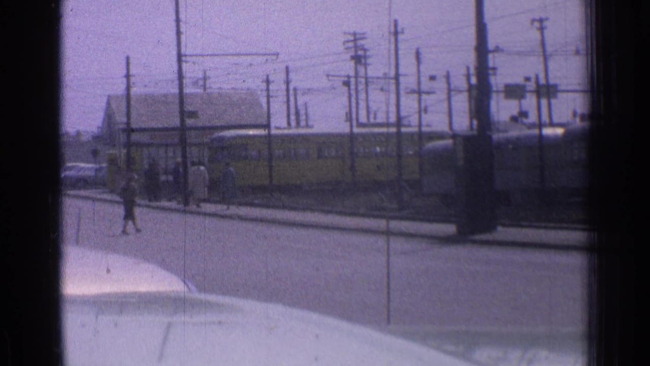 Yellow transit vehicle near a street stop with pedestrians and overhead wires.