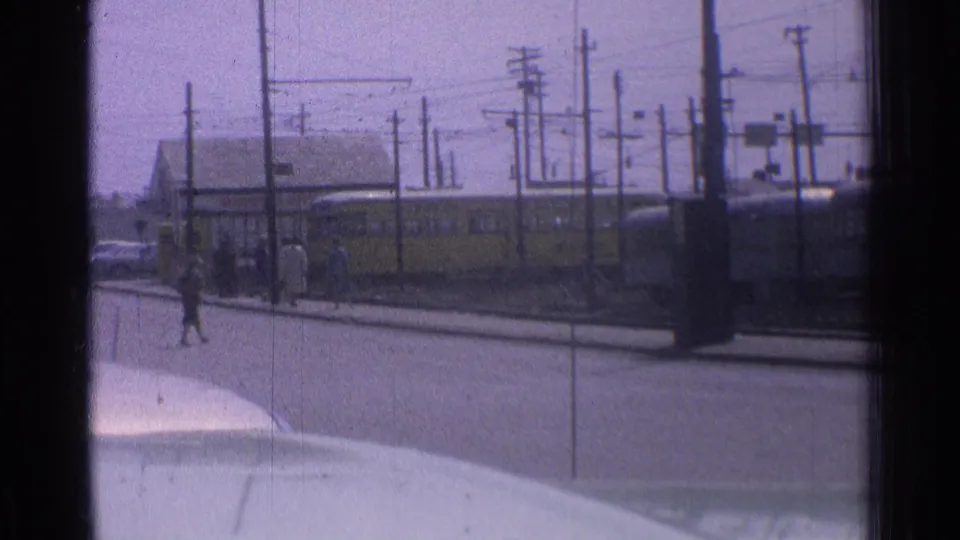 1976 Chicago street view with a yellow transit vehicle, pedestrians near the curb, utility poles, and a pale vehicle hood in the foreground.