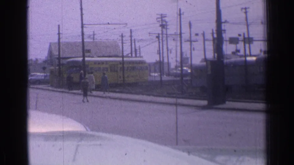 A Chicago street scene shows pedestrians near a yellow transit vehicle, with traffic signals, poles, wires, and a vehicle hood visible.