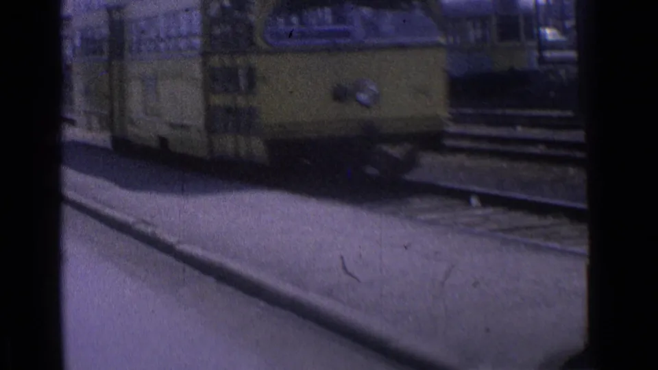 Close 1976 Chicago 8mm view of a yellow tram passing the camera, with curb, rail tracks, and street background partially visible.