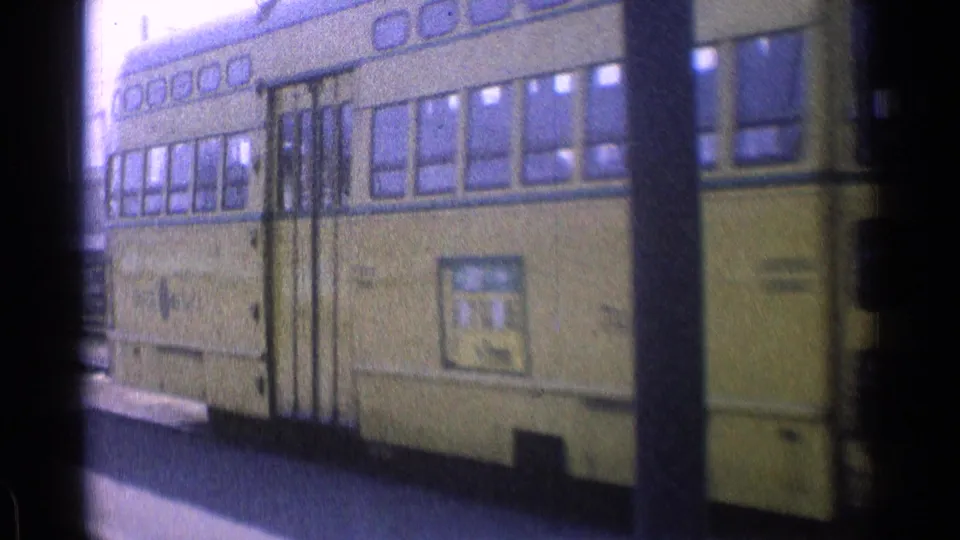 1976 Chicago frame showing the side of a yellow tram with windows, folding doors, a curb edge, and a foreground utility pole.