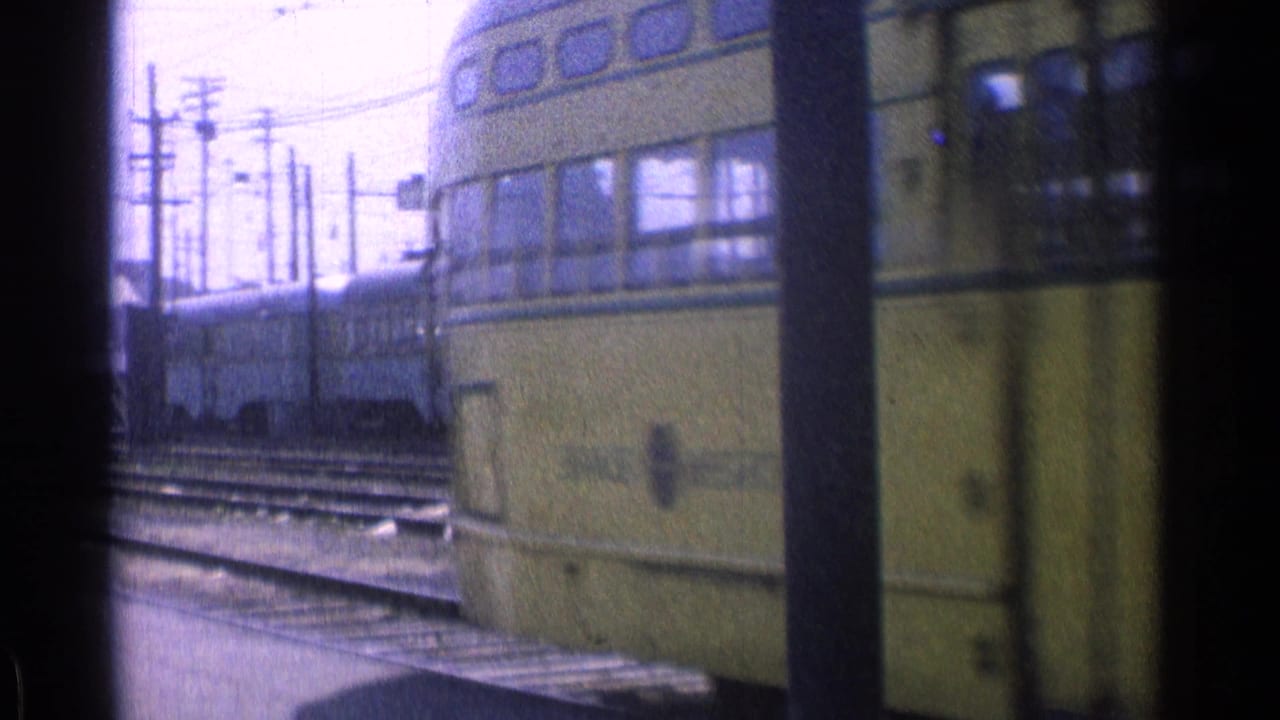 Yellow trolley car passes close beside rail tracks and utility poles.