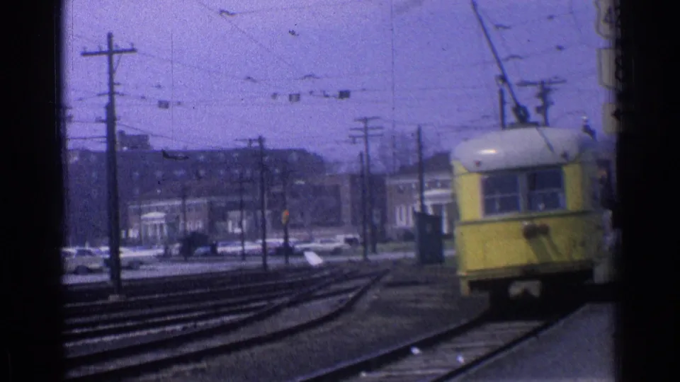 The yellow trolley continues around a curved Chicago track, framed by street signals, poles, wires, cars, and distant buildings.