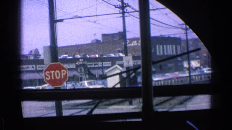 A red stop sign and commercial buildings pass outside the train windows in a 1976 Chicago urban rail view.