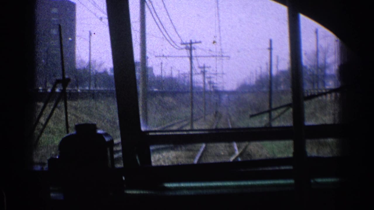 Train-window view of rails, utility poles, and overhead wires along a rail corridor.