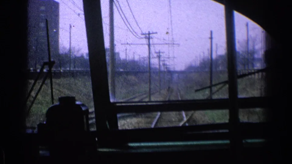 1976 Chicago train-window view showing adjacent rails, utility poles, overhead wires, and dark interior framing in the foreground.