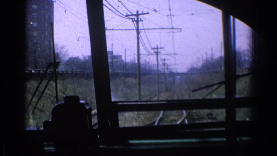 1976 Chicago passenger-train viewpoint with utility poles, overhead wires, rails, and a dark window frame enclosing the view.
