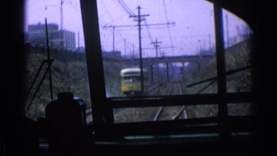 1976 Chicago rail view with a yellow train approaching on the neighboring track beneath overhead lines and near a concrete bridge.