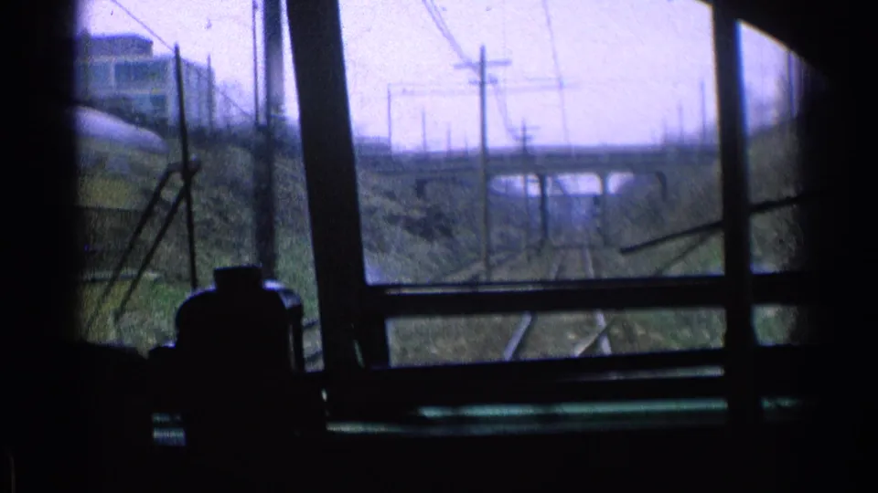 1976 Chicago train-window view looking down rails toward a concrete bridge, with overhead wires and utility poles along the corridor.