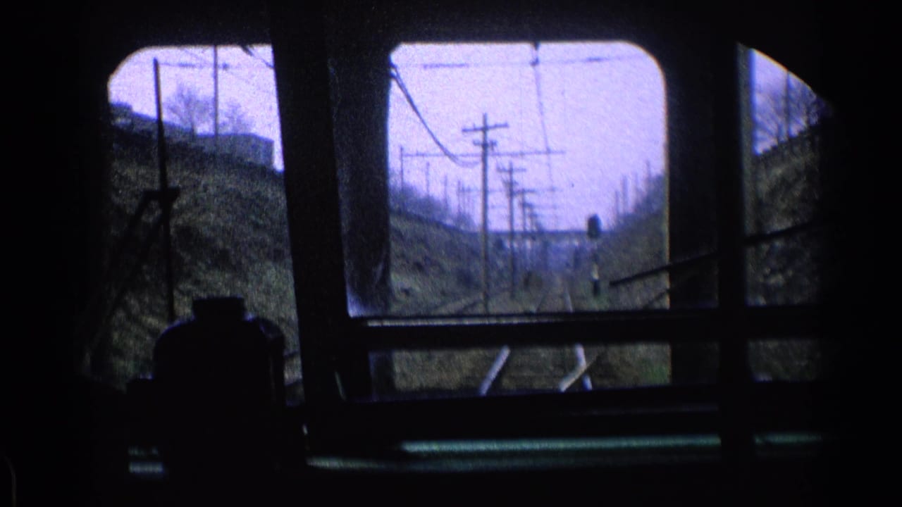Forward view from inside a train with rails, utility poles, wires, and embankments ahead.