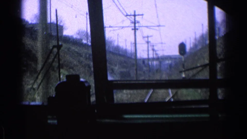 1976 Chicago rail approach seen from inside a moving train, with rails, wires, poles, and dark window hardware in silhouette.