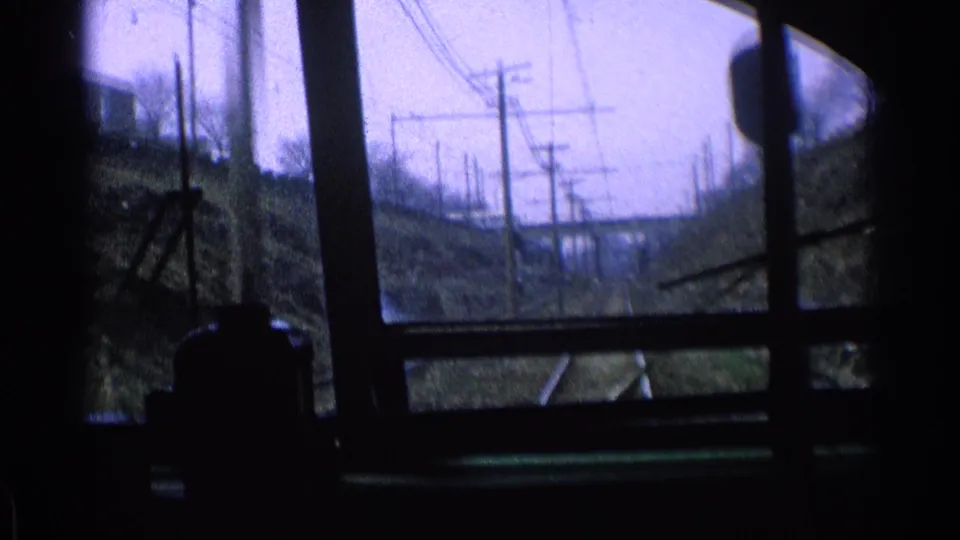 Inside-train view in 1976 Chicago, looking down tracks bordered by embankments, utility poles, and overhead lines.