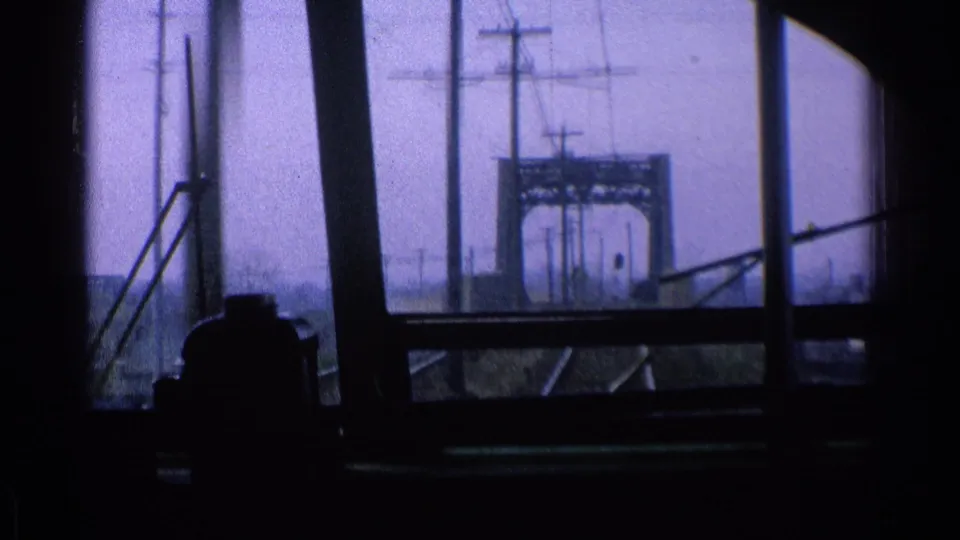 1976 Chicago view from a moving train as tracks lead toward a bridge-like overhead structure with utility poles and wires nearby.