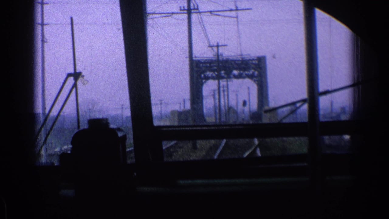 Train-window view of railroad tracks, power lines, and a steel bridge with a dark passenger silhouette.