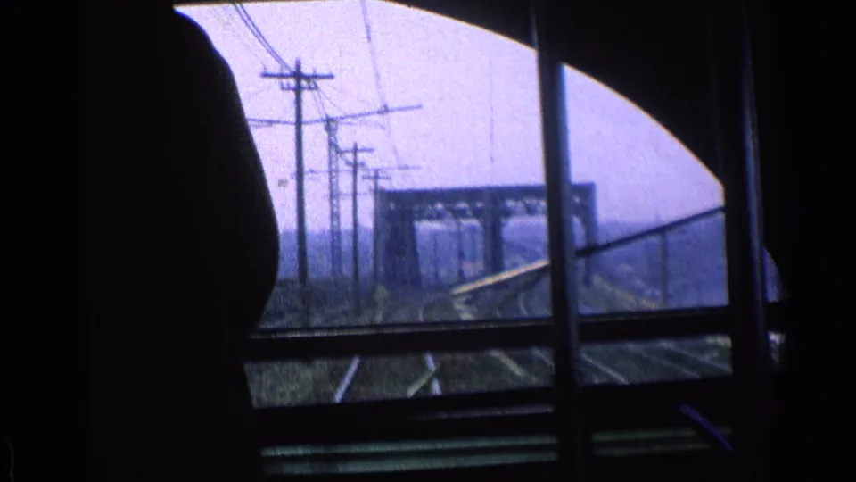 A silhouetted passenger sits or stands beside the 1976 Chicago train-window view of tracks, poles, and rail structures.