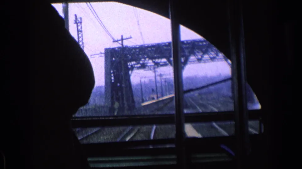 1976 Chicago rail view from inside the train, with a dark passenger silhouette and steel bridge visible through the window.