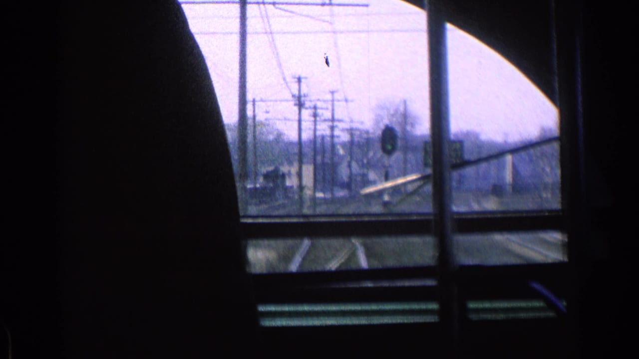 View through a train window toward tracks, overhead wires, and a distant signal.