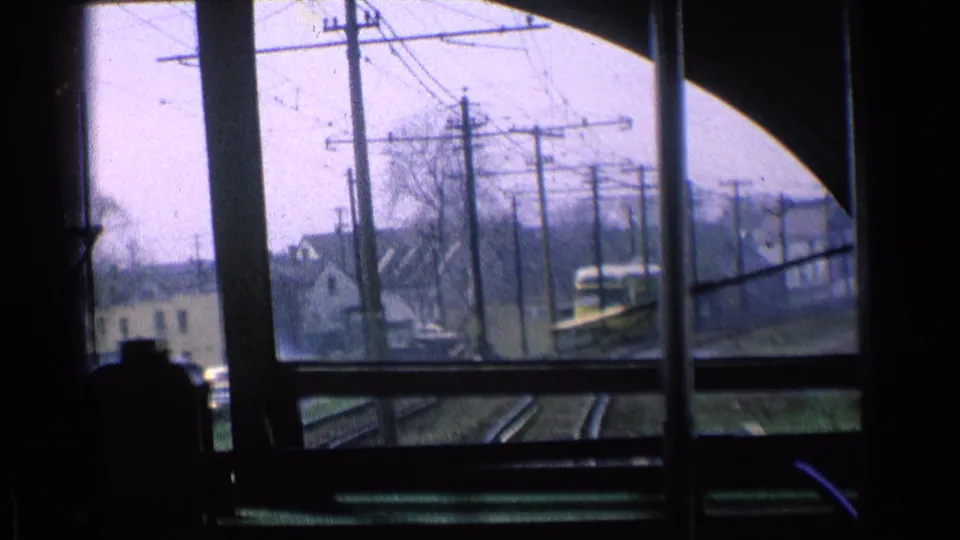 1976 Chicago rail-corridor view from inside a train, with tracks, overhead wires, houses, and a yellow train nearby.