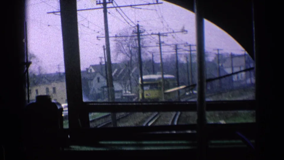 1976 Chicago footage from inside a moving train, looking past window posts toward a yellow train and residential trackside buildings.