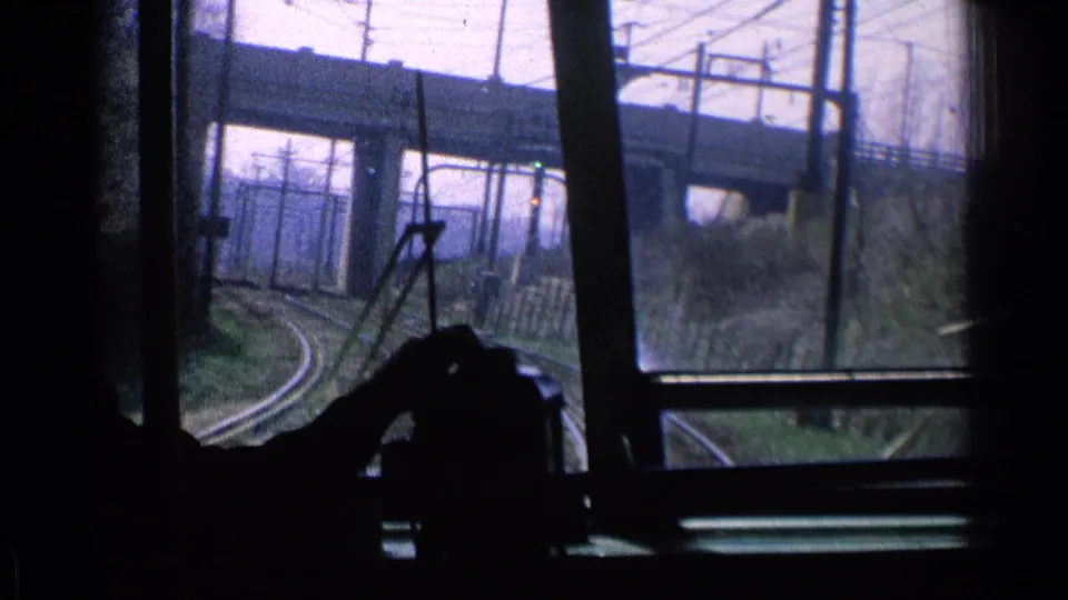 1976 Chicago train-window view with curving tracks, overhead electrical lines, a bridge, and a silhouetted passenger in the foreground.