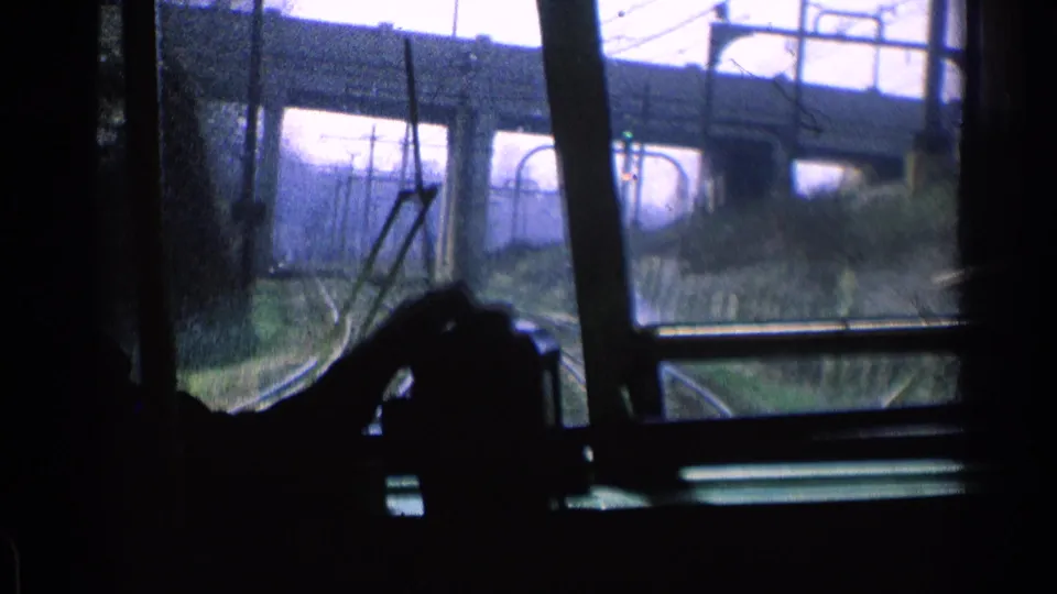 1976 Chicago home-movie frame from inside a moving vehicle, with a silhouetted hand near the wheel and power lines ahead.