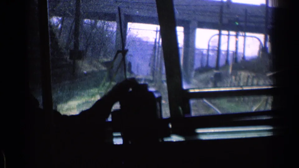 Inside-vehicle view in Chicago, 1976, showing a dark hand silhouette, windshield frame, overhead wires, and an overpass.