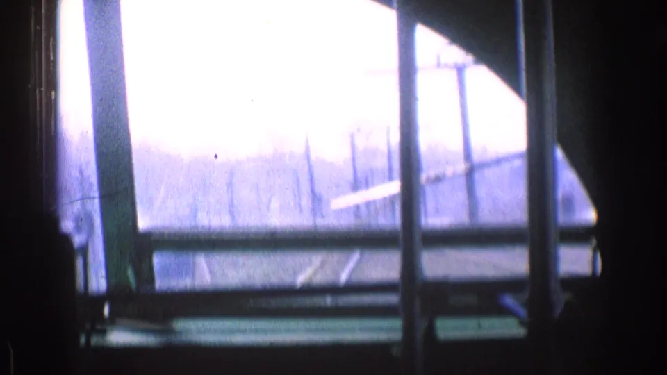 Overexposed 1976 Chicago vehicle-view frame with windshield posts, faint road edges, wires, and hazy daylight outside.