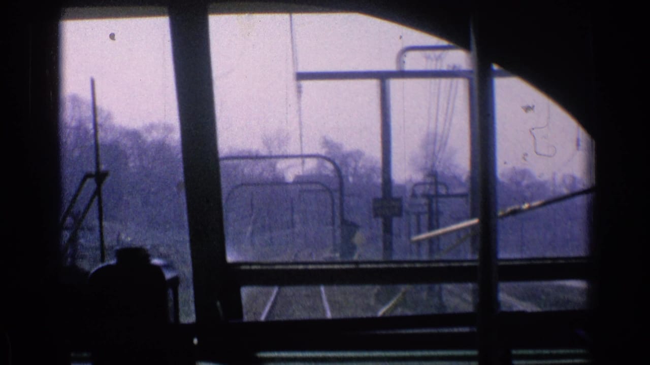 View through a transit front window toward rails, poles, and overhead wires.