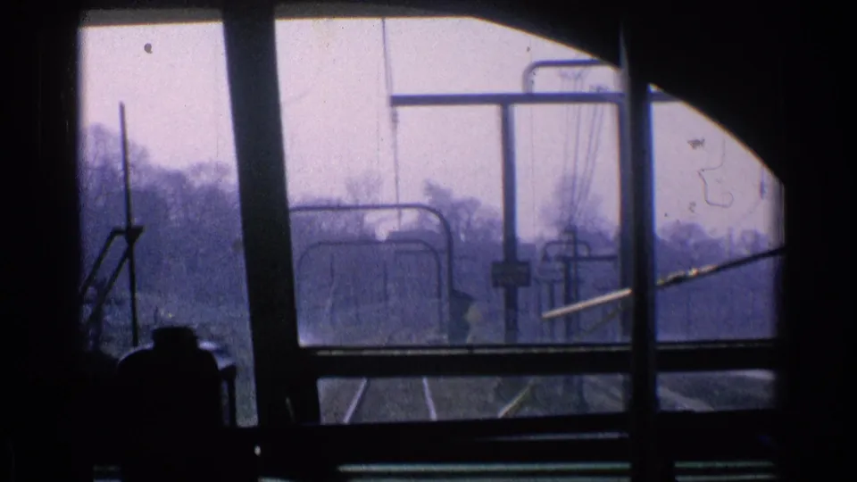 Inside a 1976 Chicago trolley or rail vehicle, the front window frames tracks, overhead wires, and a dark operator silhouette.