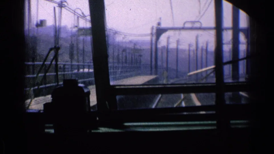 A 1976 Chicago transit view looks past the dark cab interior toward parallel rails, platform fencing, and overhead power structures.