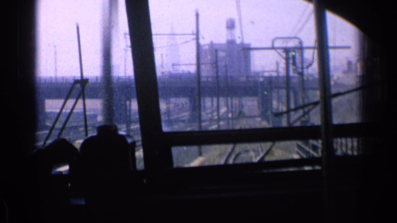 Dark train interior with passenger silhouettes and industrial rail structures seen through windows.
