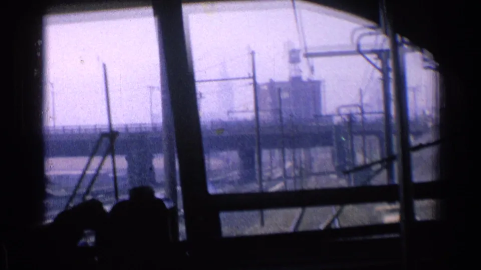 A 1976 Chicago train-window view shows industrial buildings, rail lines, and overhead structures passing beyond the dark interior.