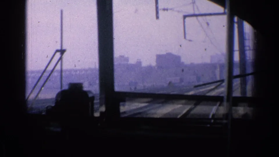 From inside the moving train, a hazy Chicago skyline and rail corridor appear beyond silhouetted seated passengers and window posts.