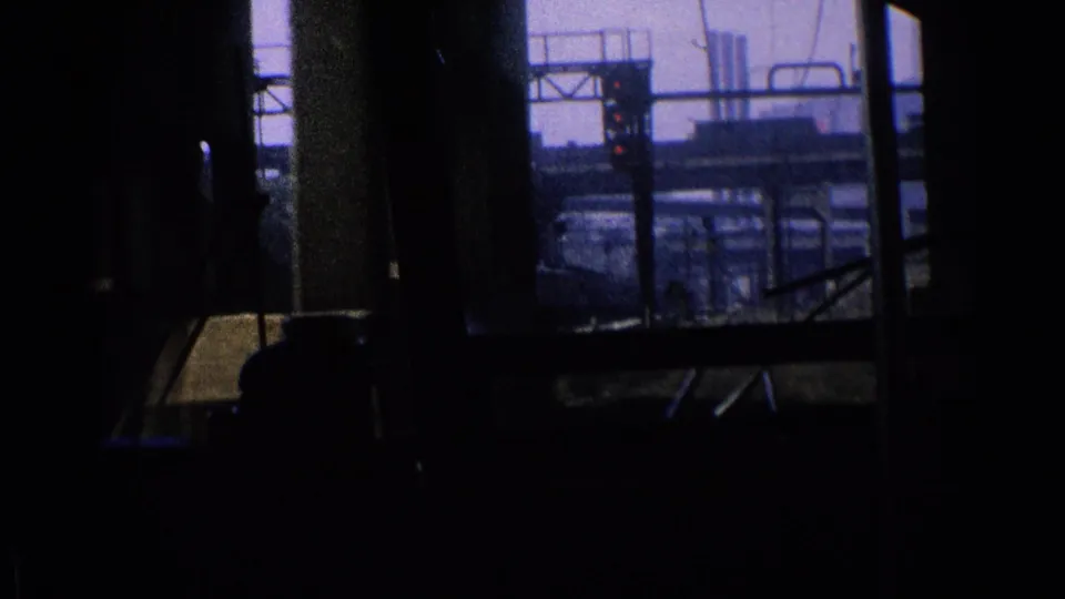 The train passes more Chicago rail infrastructure, with dark interior framing, tracks, overhead structures, and distant industrial buildings visible outside.